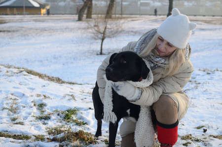 Woman in winter clothes embracing beautiful black dog on winter dayの写真素材