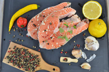 Fresh salmon steaks on black wooden surface surrounded with spices, lemon and garlicの写真素材