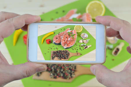Hands with cell phone taking photo of fresh salmon steaks surrounded with spices ready for grillの写真素材