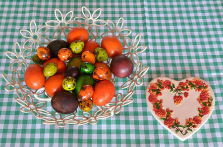 Basket with colorful Easter eggs on green-white table cloth and ceramic heart as decoration