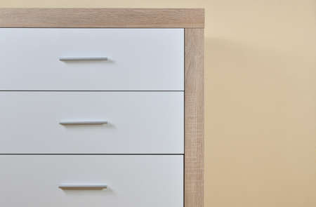Chest of drawers made of wooden materials with beige wall beside itの写真素材