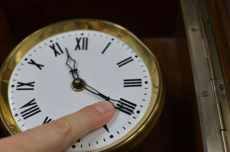 A finger on a hand of a vintage clock trying to stop it or trying to turn back timeの写真素材