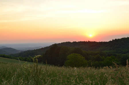 Sunset over spring meadows and hills with lush treesの写真素材