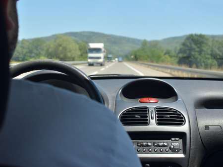 Man driving a car with a dirty front glass after a long drive on a highway and a white truck blurred...