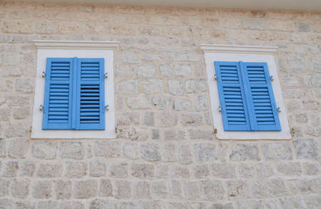 Two windows with blue wooden jalousies on a coastal house facade