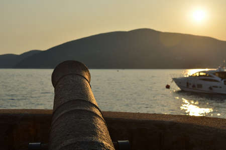 Old cannon directed to a sea and a distant land in sunsetの写真素材
