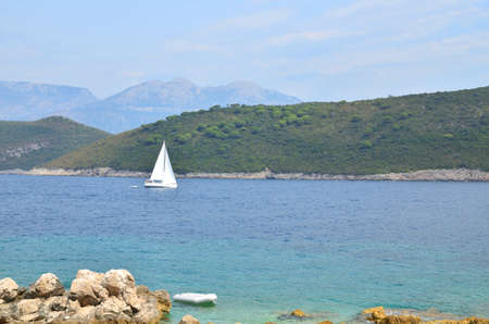Wavy sea with sailing boat in bay, with hills in distanceの写真素材