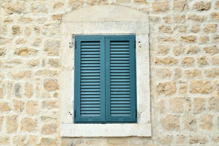 Window shut with wooden blinds of a coastal stone houseの写真素材
