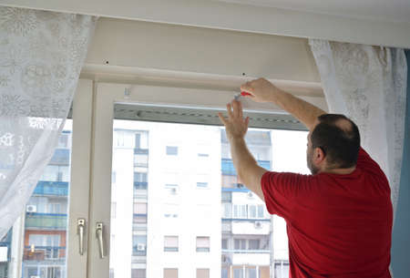 Man measuring and marking a position of a hole in order to install a blind. A part of residential...