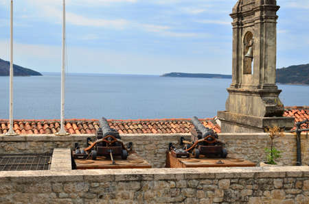 Belfry and cannons as parts of a medieval city fortification as a protection against attacks coming from sea with a blue sea and a coastの写真素材