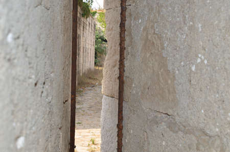 Paved alley in an abandoned fortress seen while peeking through two wallsの写真素材