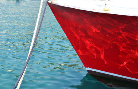 Bow of a moored red boat in a blue seaの写真素材