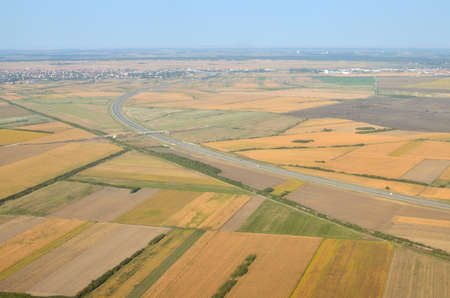 Plains with different crops and plants, highway and a city suburb seen from a landing plane