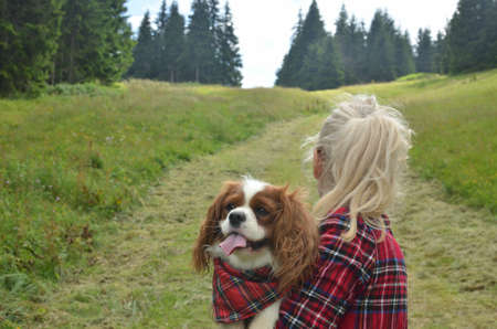 Woman dressed in royal stewart hiking with her dog - Cavalier King Charles Spaniel - having a collar with a same pattern hiking on mountain pathの写真素材