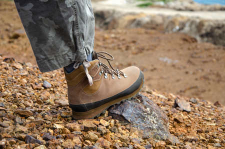 Foot in hiking shoe on a stone and surface of orange dust and soil
