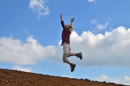 Happy woman, dressed in royal stewart, jumping against the blue sky with white cloudsの写真素材