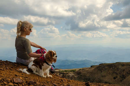 Woman and her dog, Cavalier King Charles Spaniel, are watching picturesque mountain landscapeの写真素材