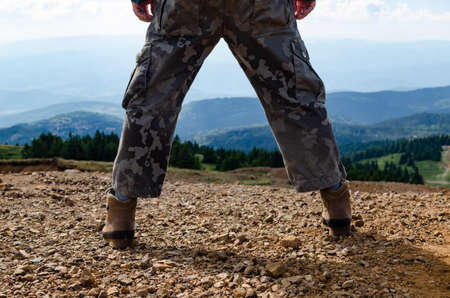 Man dressed for hiking, standing with spread legs on top of Kopaonik mountain in Serbia and watching landscapeの写真素材