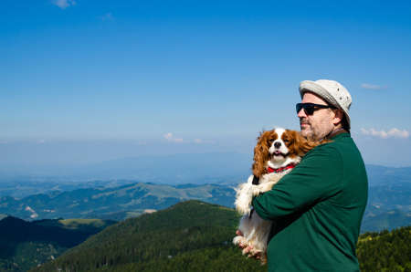 Man holding his dog - Cavalier King Charles Spaniel - in a mountain landscapeの写真素材