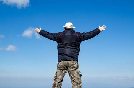 Man with spread arms in a joyful pose, with blue sky againstの写真素材