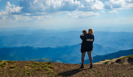 Woman holding her dog on a mountain top, watching a landscape. Translation of the text on the jacket: "Serbia".の写真素材