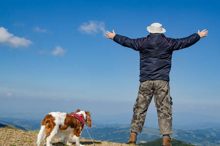 Man with spread arms in a joyful pose, with his dog in a mountain landscapeの写真素材