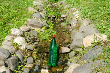 Green plastic bottle of water in a brook on a sunny dayの写真素材