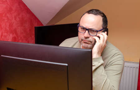 Businessman by a computer talking on the cell phone, with a face gesture showing full concentration...