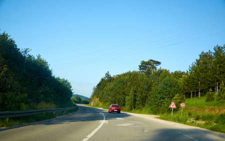 Red car on a road, driving through an countryside landscape