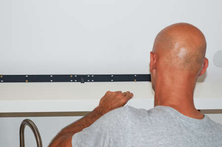 Man attaching a shelf on a shelf holder on a wall - close-up