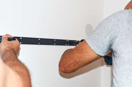 Men's hands screwing a shelf holder with a screw gun on a wall - close-up