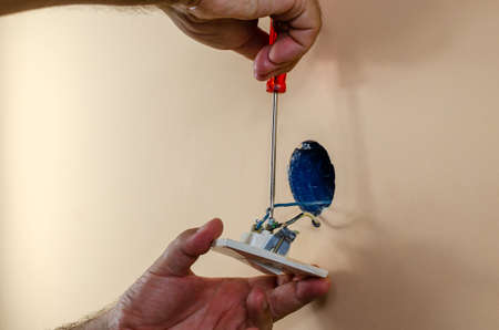 Fixing old light switch on a wall with a screwdriver