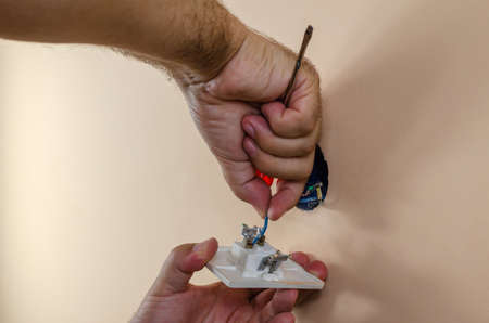 Man's hands detaching electric wires from an old light switch