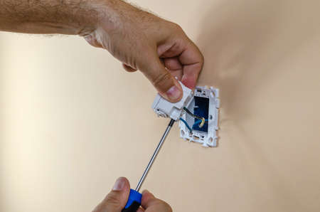 Connecting electric wires to a modular light switch on a wall with a screwdriverの写真素材