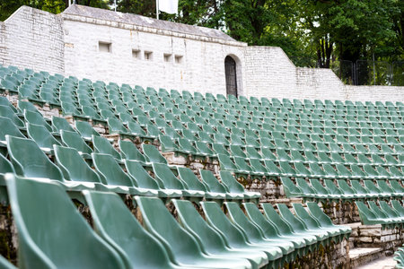 Large, open-air stone amphitheater is filled with numerous rows of green plastic seats arranged in a semi-circular patternの写真素材