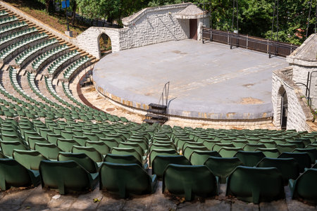 Amphitheater with concentric rows of tiered seating curving around a central stage area under an...
