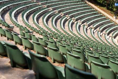 Large, open-air stone amphitheater is filled with numerous rows of green plastic seats arranged in a semi-circular patternの写真素材