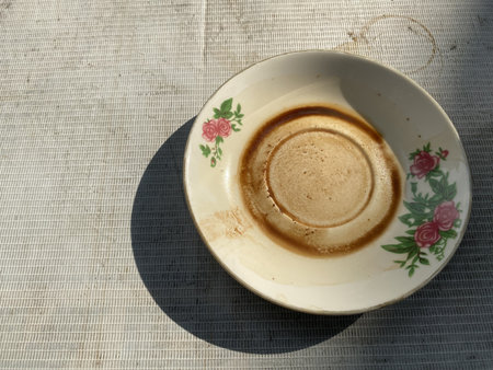 Dirty teacup saucer with floral decoration and shadow on a textured surface.