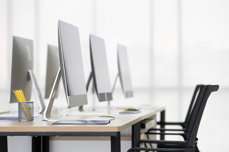 Group of new computers on desk in modern office with windows in background