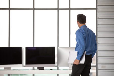Young Asiabn businessman standing and holdin new laptop computer with happiness manner in modern office, group of desktop computers blur in behide.の写真素材