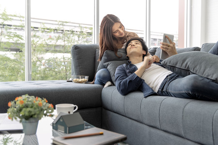 Asian teenage couple make eye contact relaxing on a sofa  by the window relax in the luxurious room.