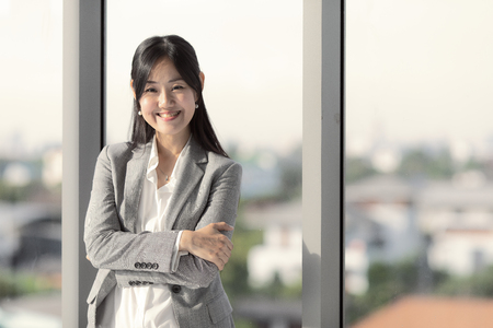 Asian long-haired businesswoman looks good in suit smiling Stand with confidence in the office window.の写真素材
