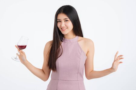Attractive young asian woman in pink dress, holding her drink and happy at fun party, portrait on white background with colorful festive balloons.の写真素材