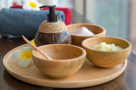 Closeup shot of Thai massaging stuffs herbal towel compress ball, coconut oil, perfume, cosmetics and plumeria flower in wooden tray placing on massage bed in spa therapy preparing for customer.の写真素材