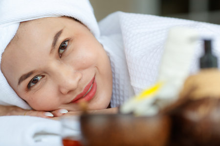 Close up facial shot of Asian happy female model in white clean bathrobe lying down closed eyes...