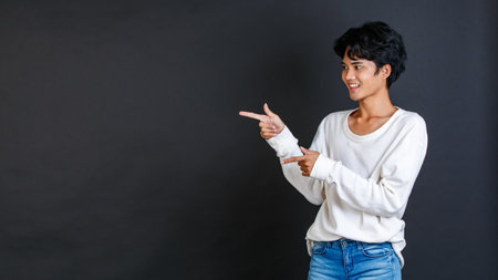 Studio closeup shot of Asian young LGBTQ gay glamour bisexual homosexual male model in casual outfit standing smiling holding two hands and fingers pointing blank copy space on black background.の写真素材