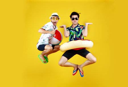 Two young Asian guys in summer casual with hat and sunglasses jumping up high with funny gesture...