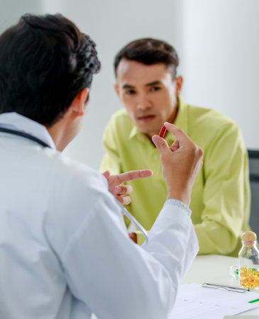Professional physician pointing to medicine capsule and asking for illness symptom to Asian patient to diagnose sickness and guiding pharmacy for disease treatment at health care center of hospital.の写真素材
