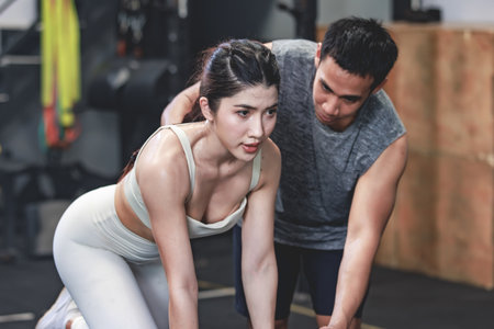 Asian professional muscular male personal trainer teaching female fit strong body sporty athletic fitness model in sport bra legging and gloves lifting dumbbells exercising triceps in CrossFit gymの写真素材