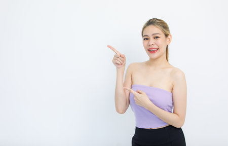 Portrait isolated cutout studio shot of Asian beautiful pretty cheerful female model in tube cropped top shirt smiling look at camera holding hands pointing fingers on copy space on white background.の写真素材
